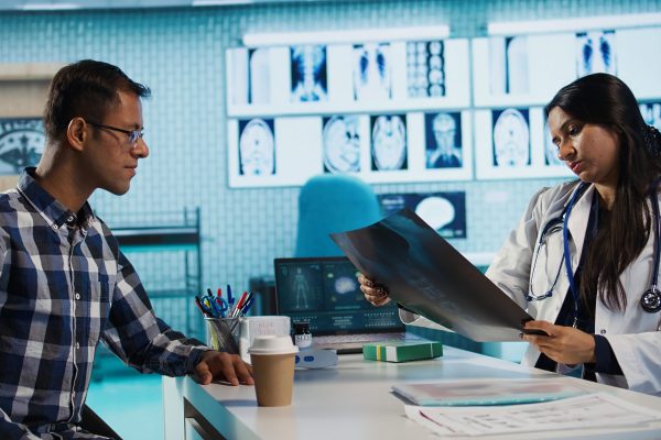 Indian general practitioner and patient engage in a medical consultation with diagnostic tools and x ray text results for scan interpretation. Showcasing healthcare practices and research. Camera B.